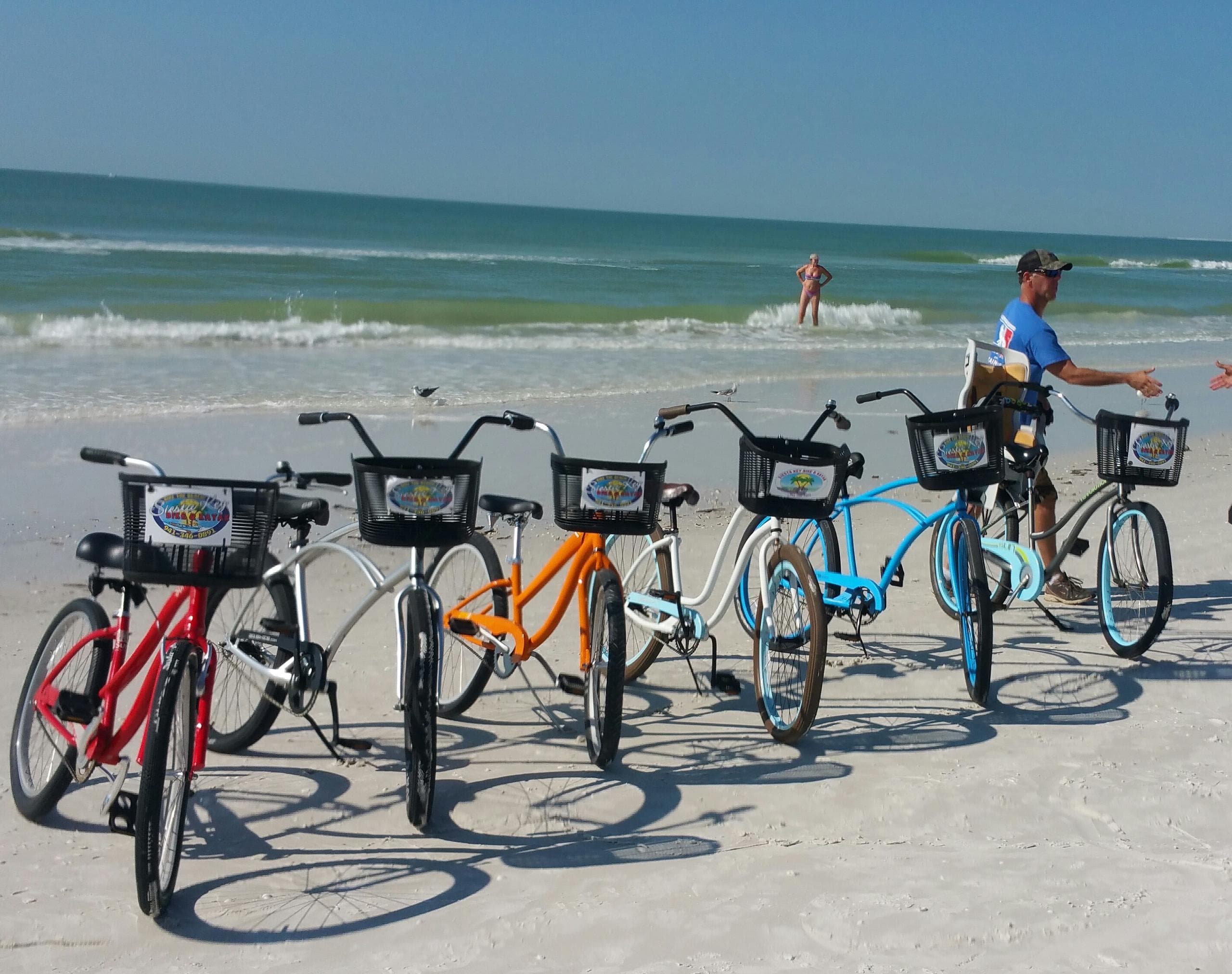 Colorful rental beach bikes lined on sandy shore by blue ocean