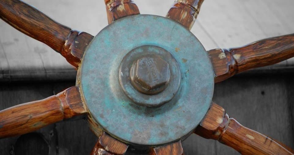 Wooden ship wheel close-up on classic sailboat helm in harbor