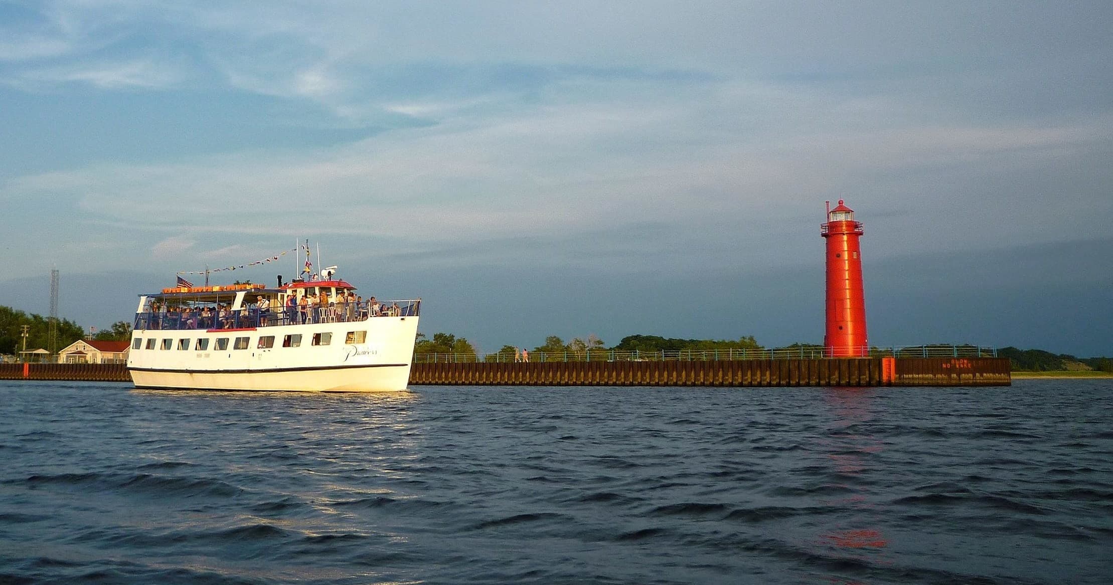 Sightseeing cruise boat near red lighthouse on calm sea