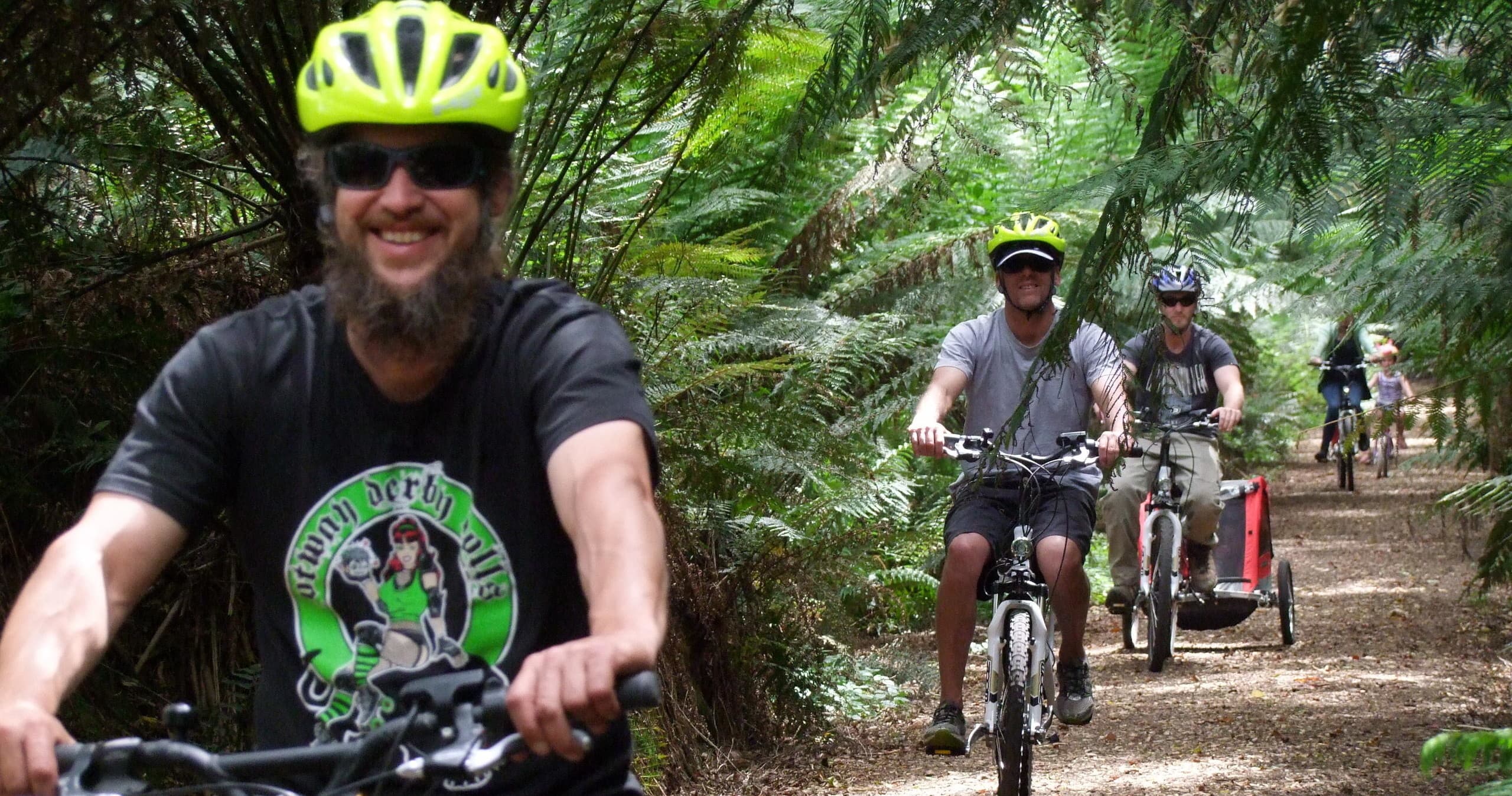 Lead cyclist on e-bike with group riding lush fern forest trail
