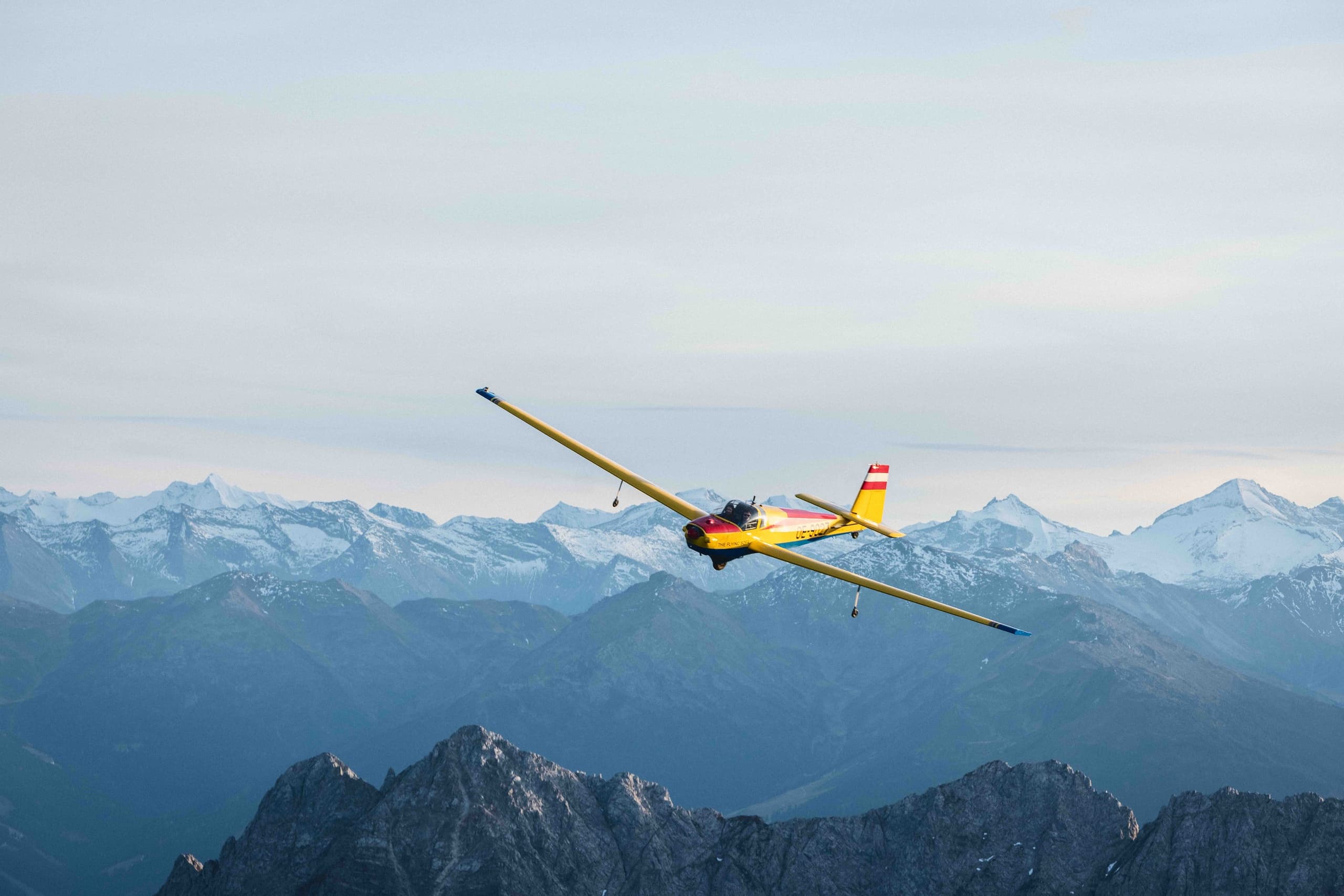 Yellow glider soaring above distant mountain range in daylight