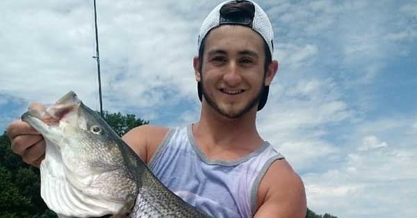 Angler holding large bass on lakeshore after successful catch