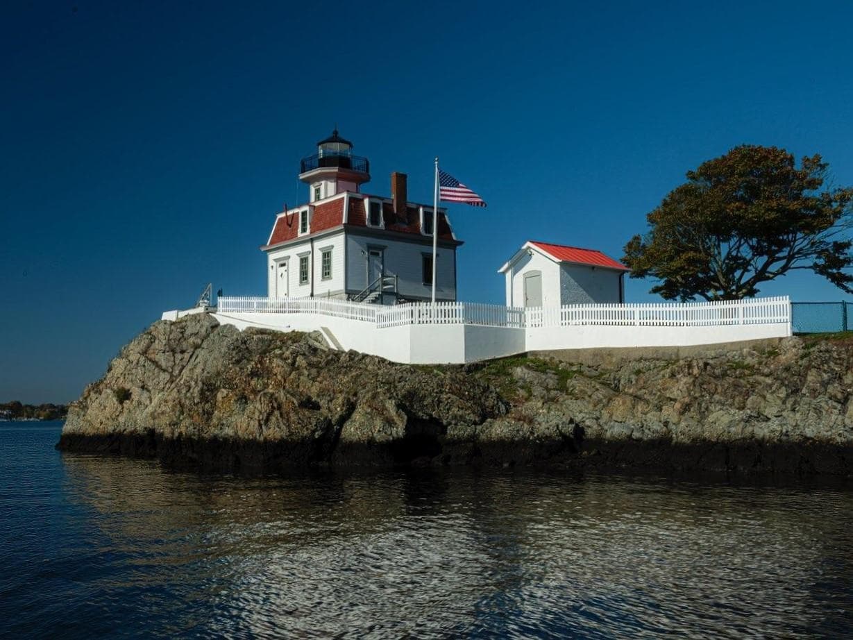 Pomham Rocks Lighthouse and keeper's house lit at dusk over harbor