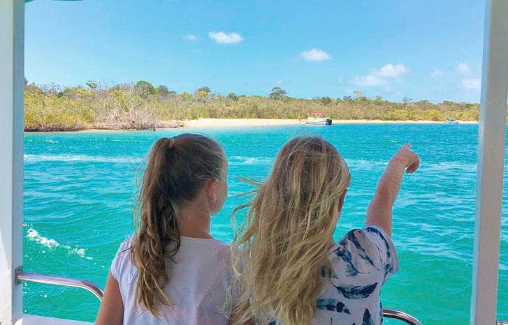 Children pointing toward shoreline on family Noosa canal cruise