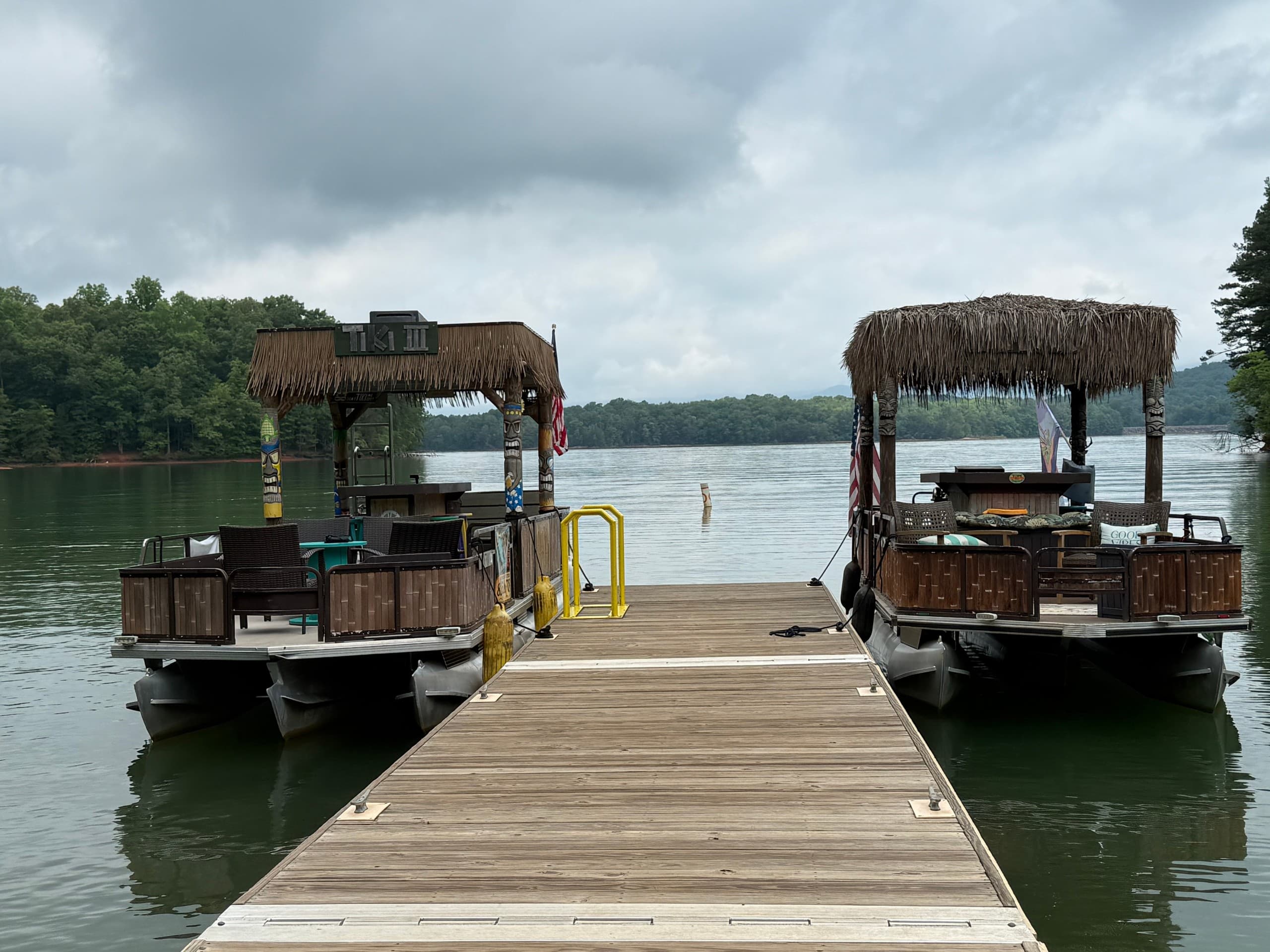 Wooden dock leading to tiki pontoon boats on peaceful lake
