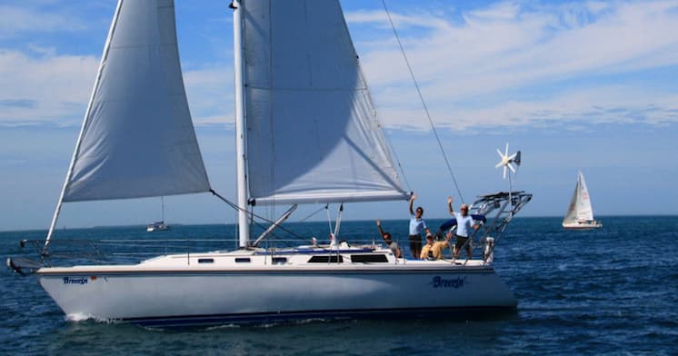 Crew sailing on white yacht in open ocean under blue sky