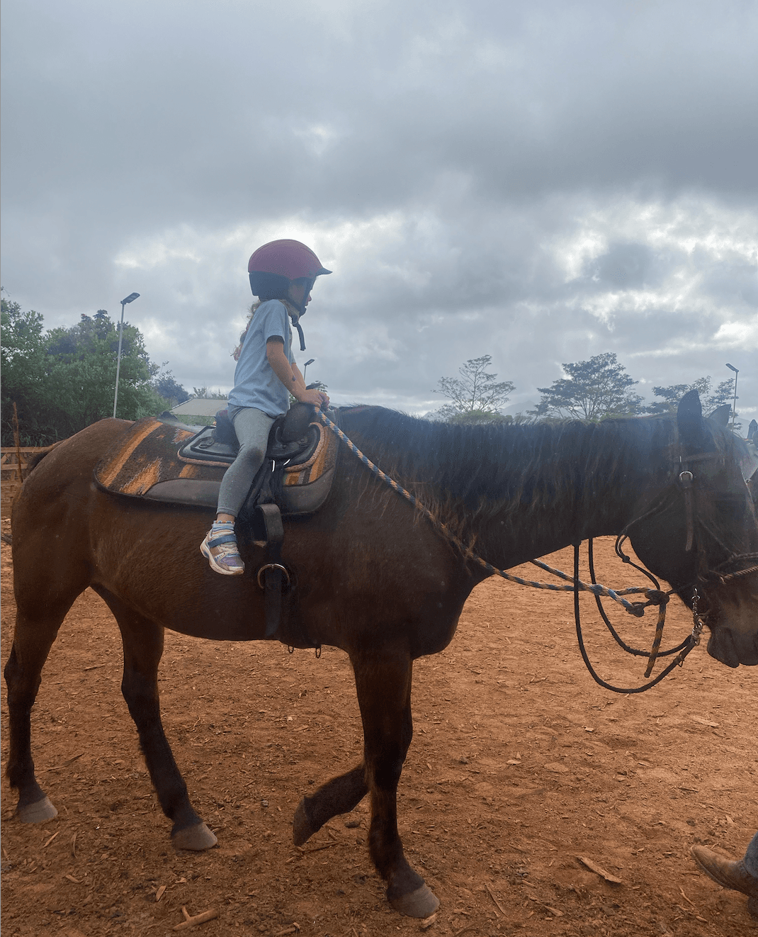 Young child riding horse at Hawaiian ranch arena under clouds