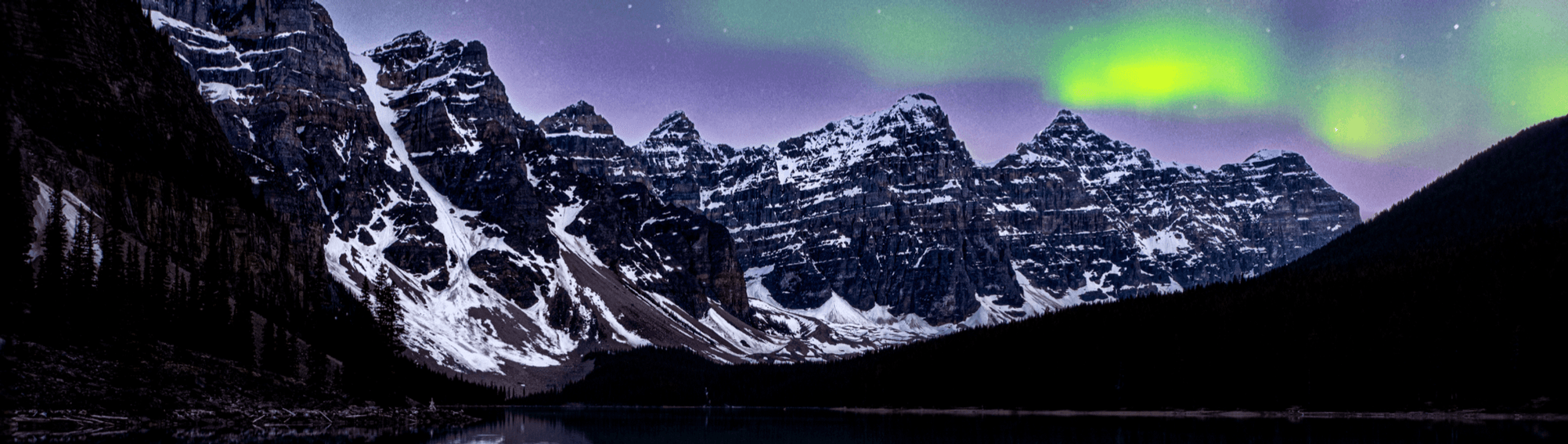 Northern lights over snow-capped mountain range at lakeshore panorama