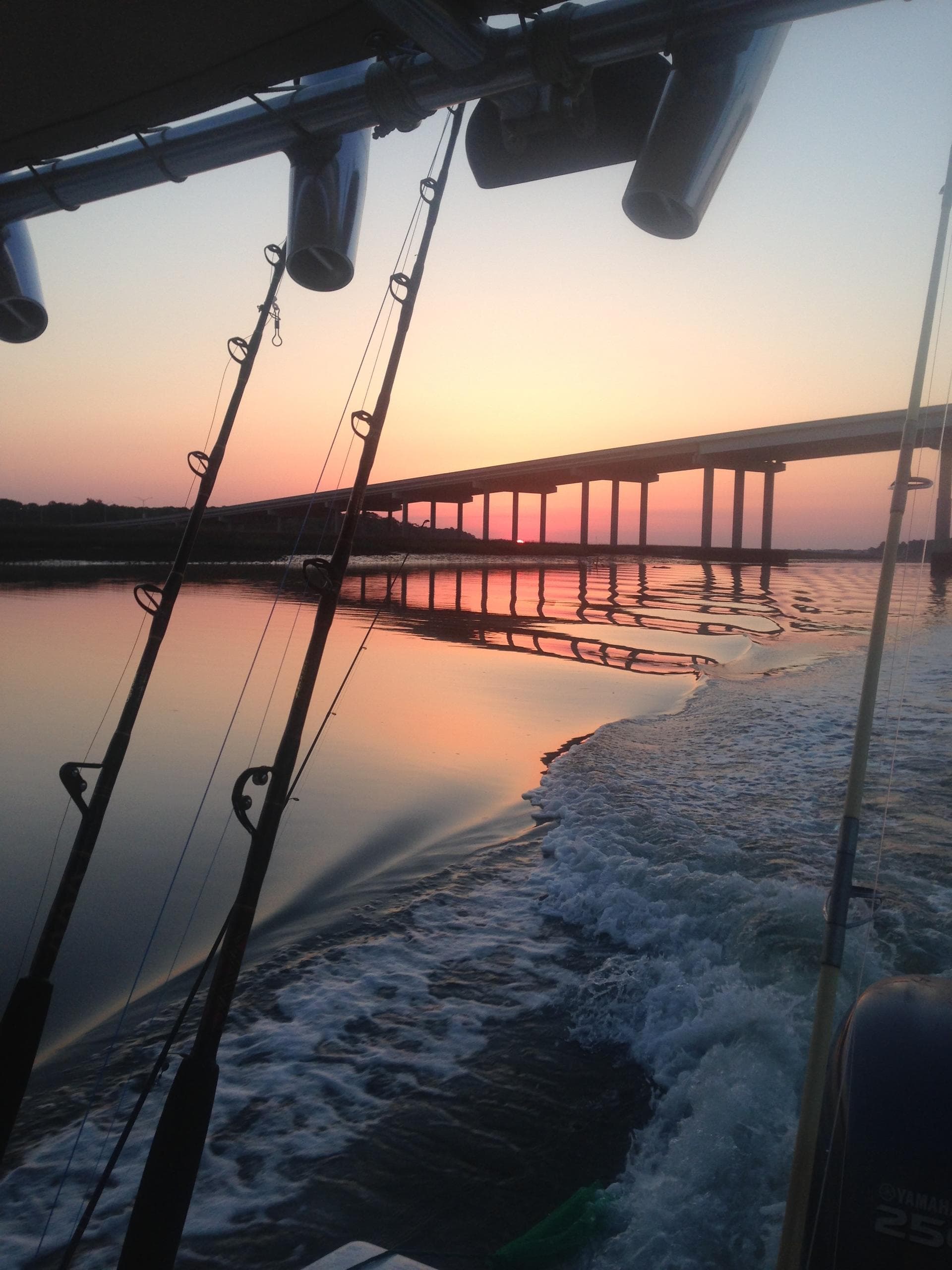 Fishing rods and wake from a charter boat under a bridge