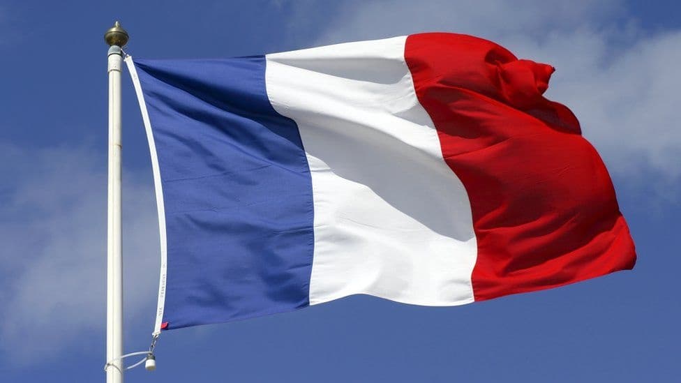 French flag waving against blue sky, reflecting regional heritage