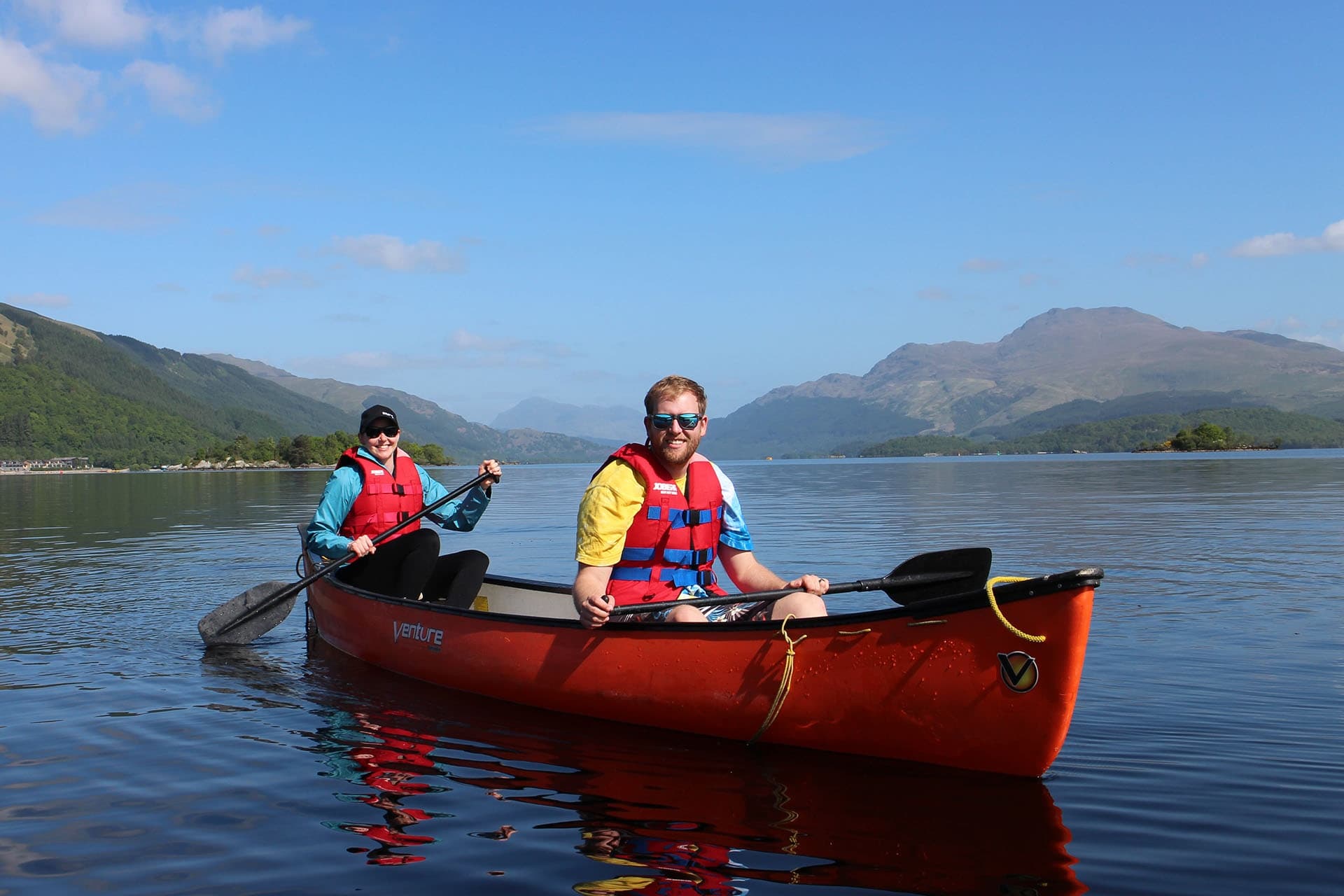 Couple canoeing on calm Loch Lomond with mountain reflections