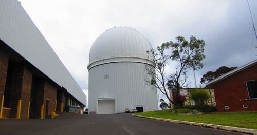 Ground-level view of white dome observatory beside campus buildings