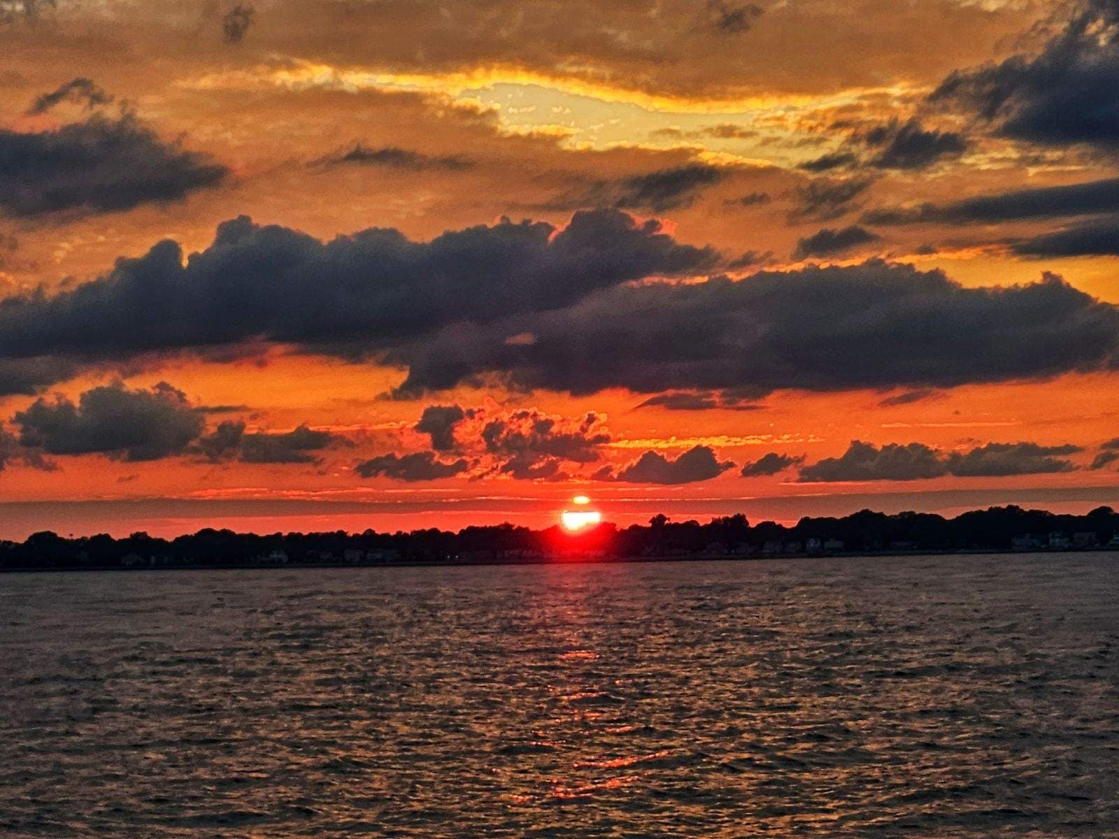Dramatic sunset over open water on coastal harbor skyline