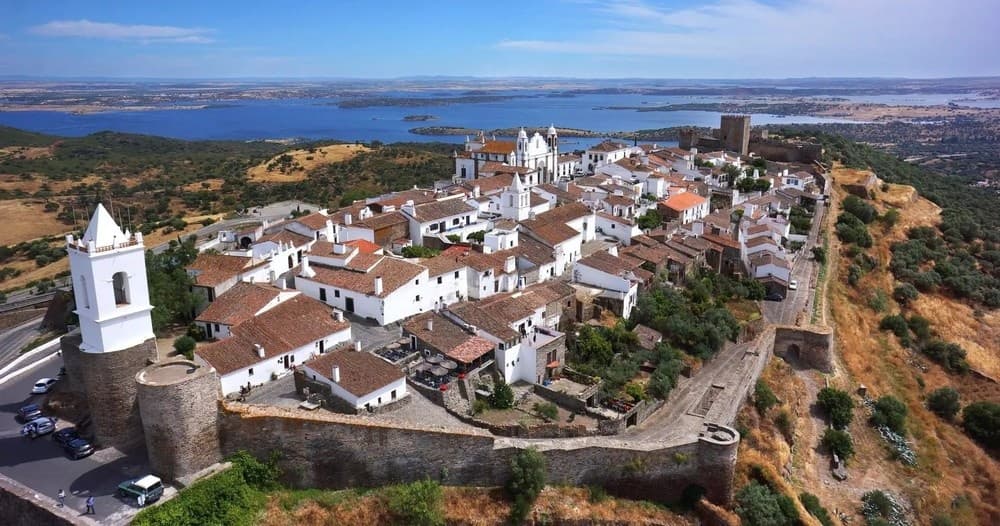 Wide aerial of fortified white village on hilltop, coastal views