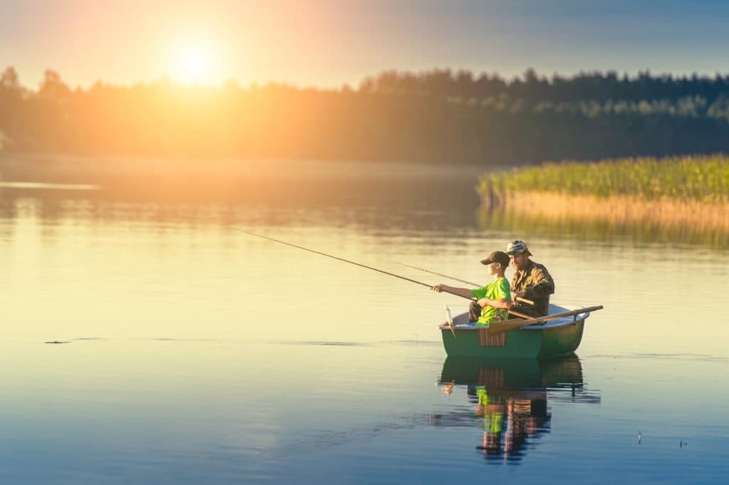 Angler fishing from small boat at sunrise on tranquil lake