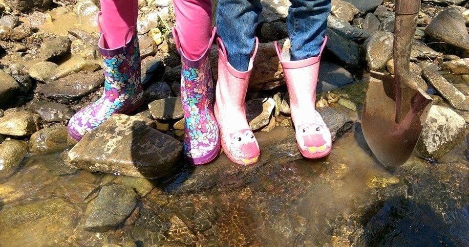 Children in colorful rubber boots splashing in a shallow creek