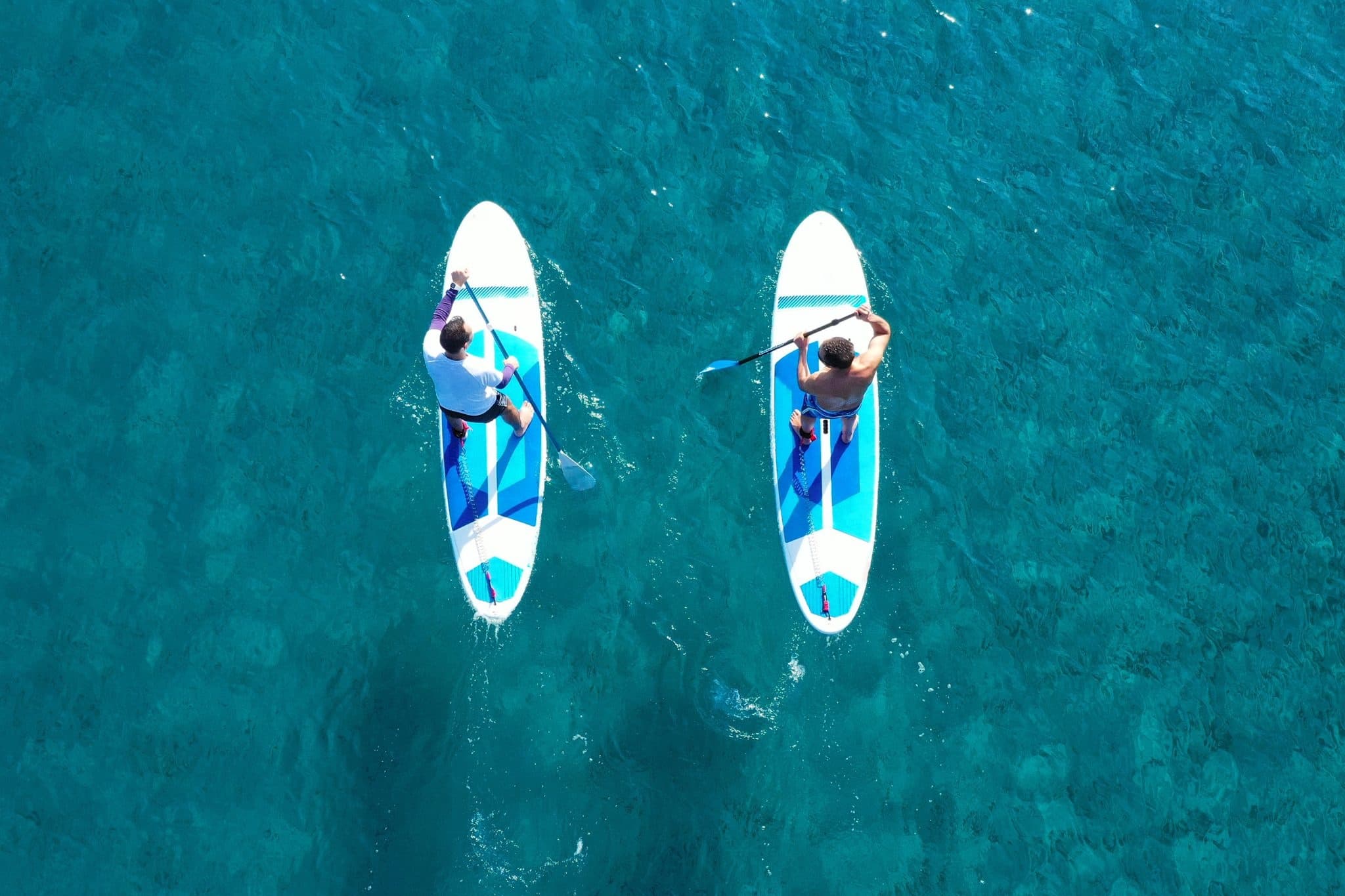 Two paddleboarders paddling over turquoise sea from aerial view
