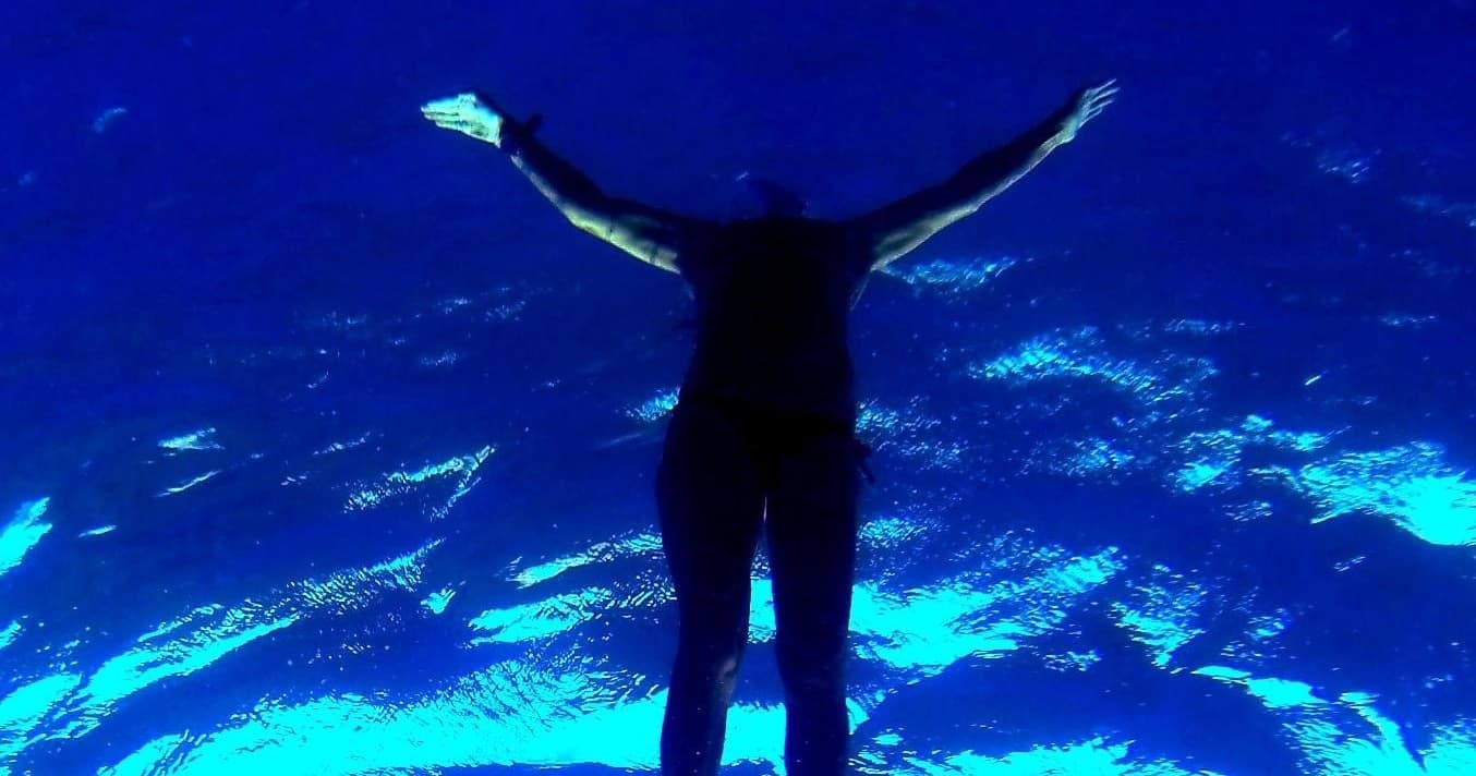 Freediver silhouetted against deep blue ocean underwater cave
