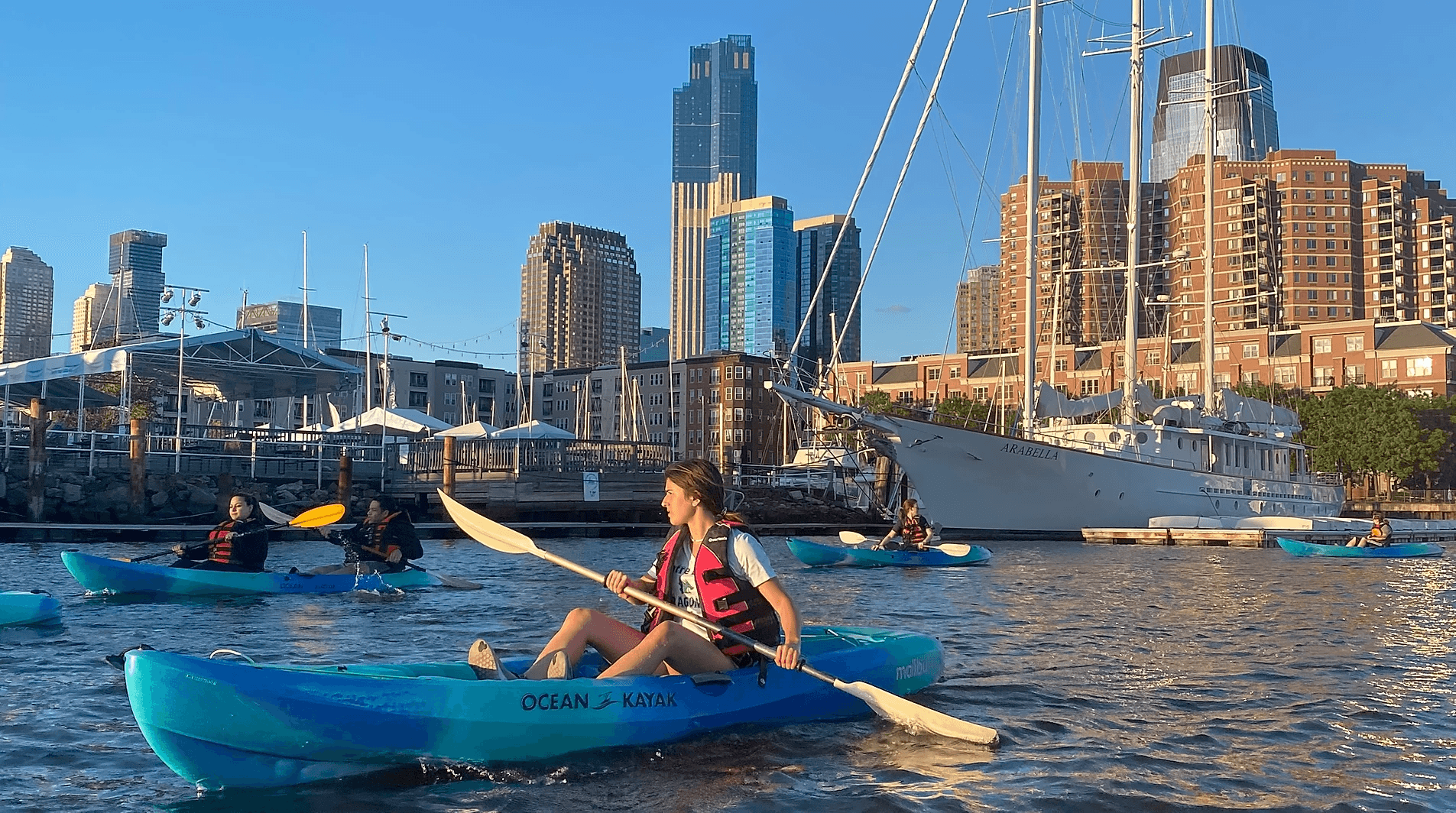 Kayakers paddling near city harbor with sunset skyline view