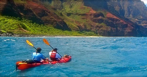 Two kayakers paddling along the dramatic Nā Pali Coast cliffs, Kauai