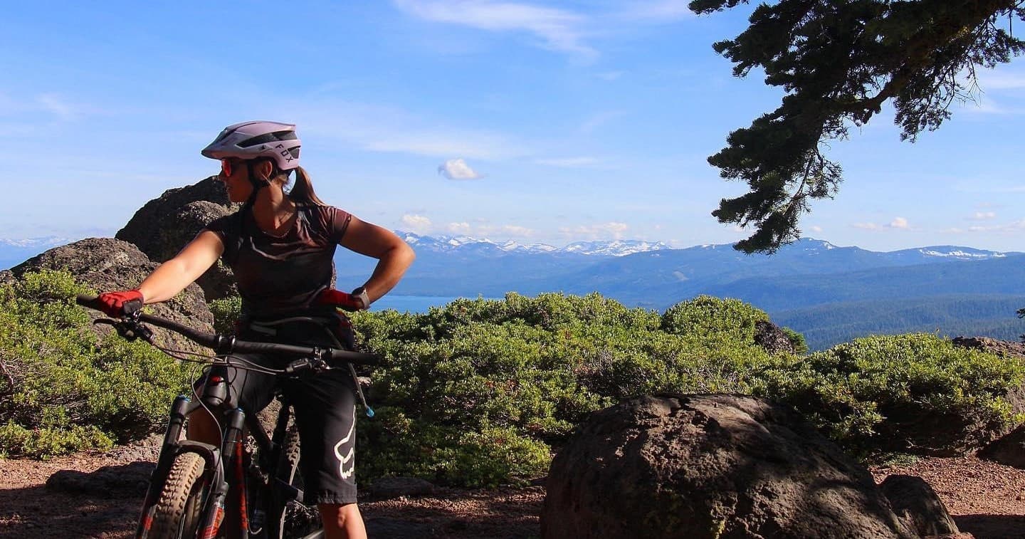 Solo mountain biker pausing on rocky Tahoe ridge with panoramic view