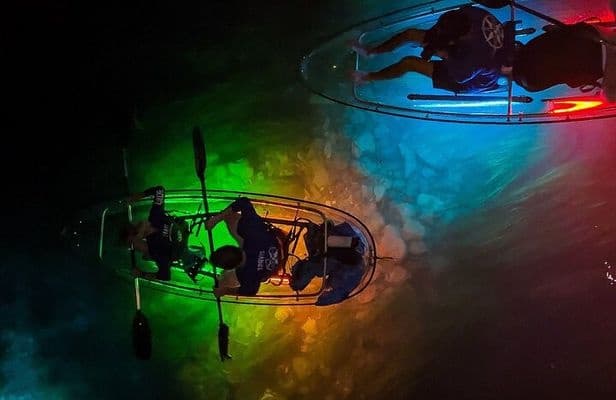 Transparent kayakers paddling over illuminated tropical lagoon