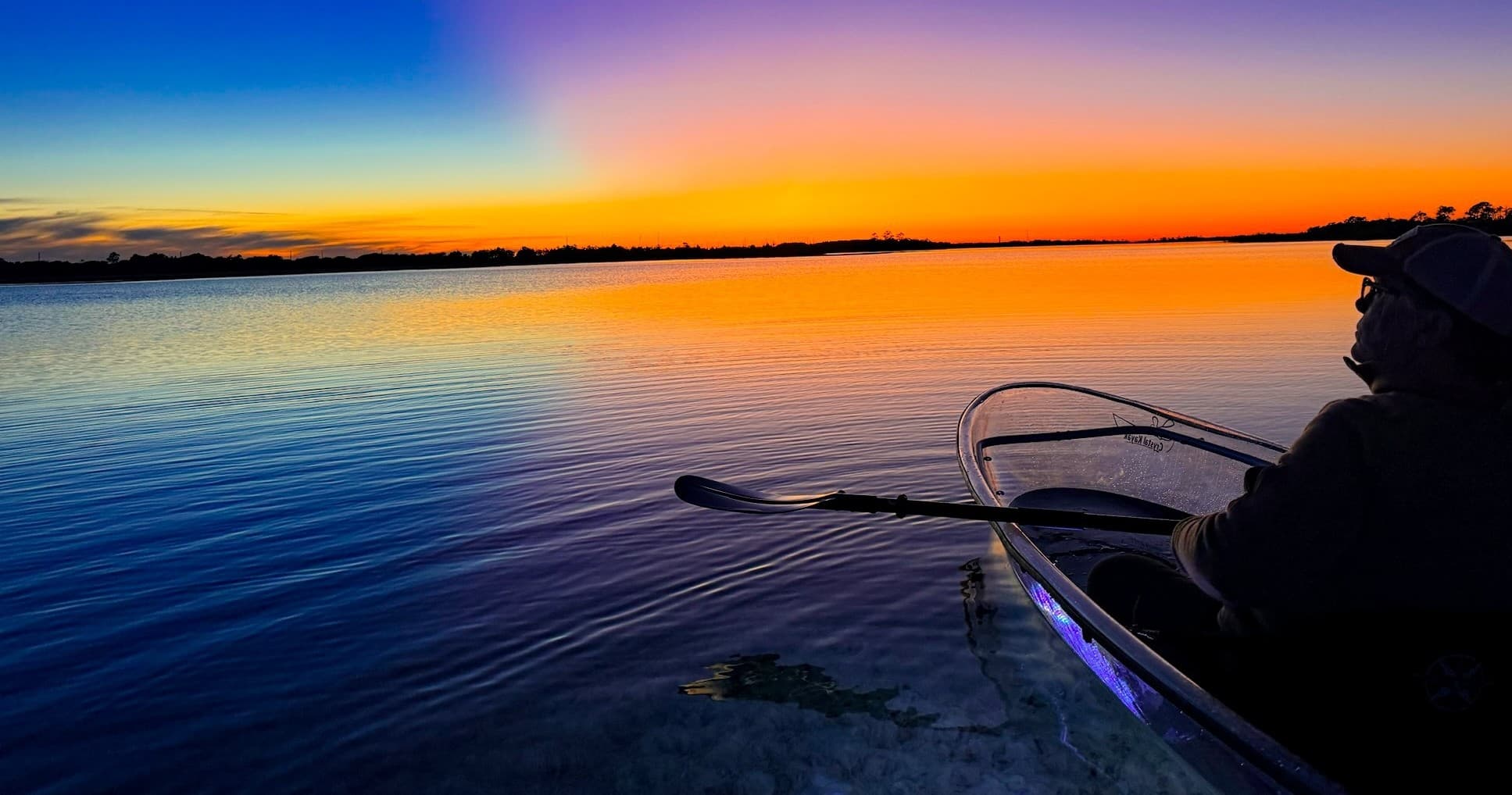Clear kayak at sunset over calm Gulf coast, silhouetted paddling