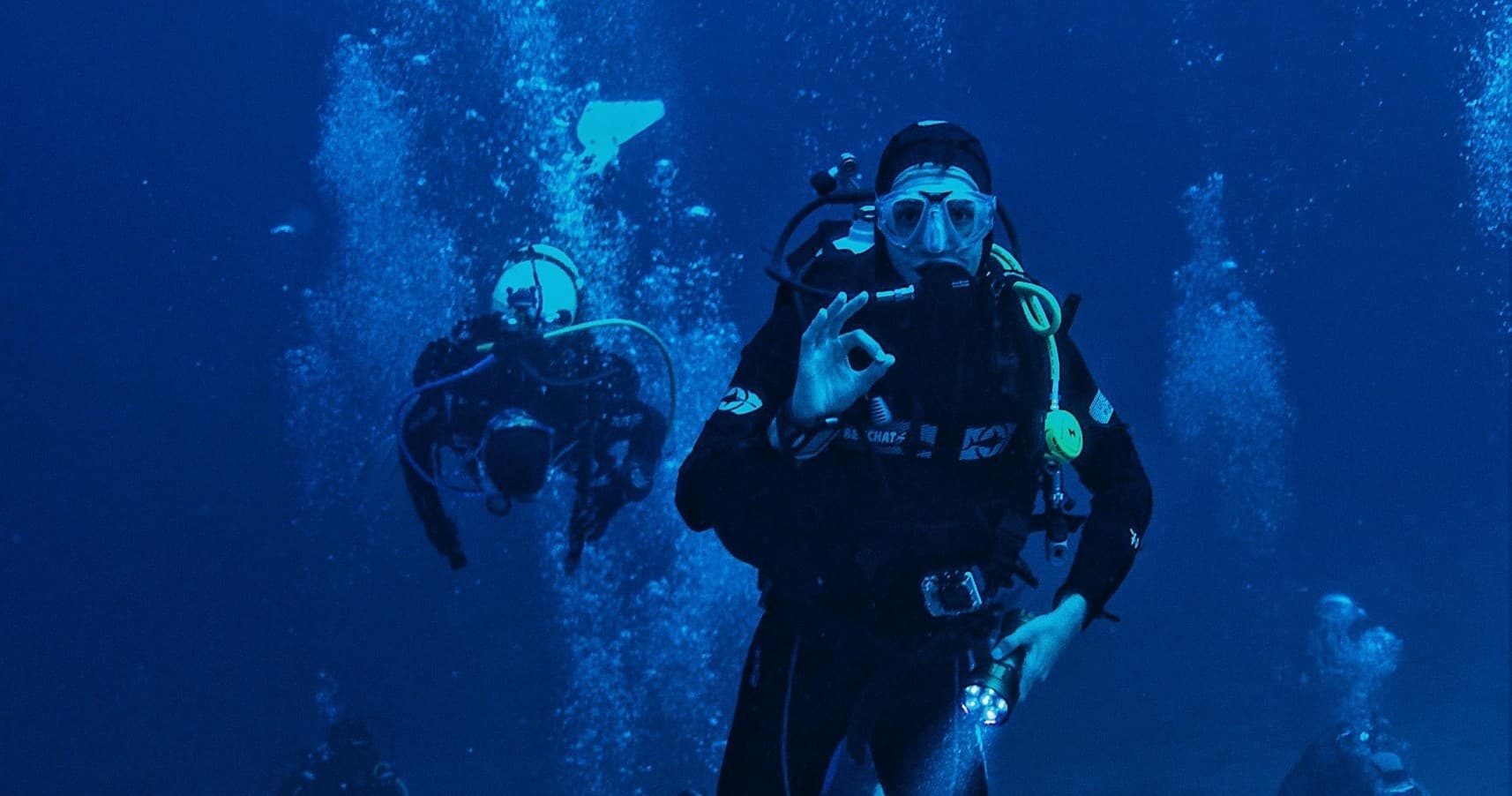 Group scuba dive in deep blue ocean with divers ascending