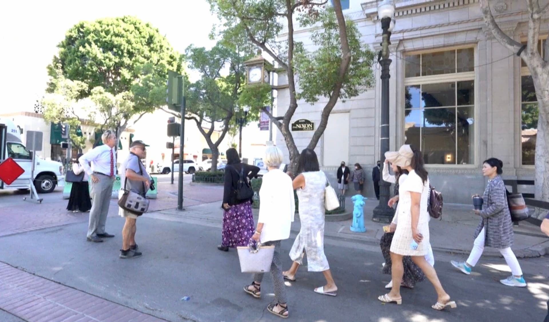 Group of pedestrians walking on sunny downtown street with trees