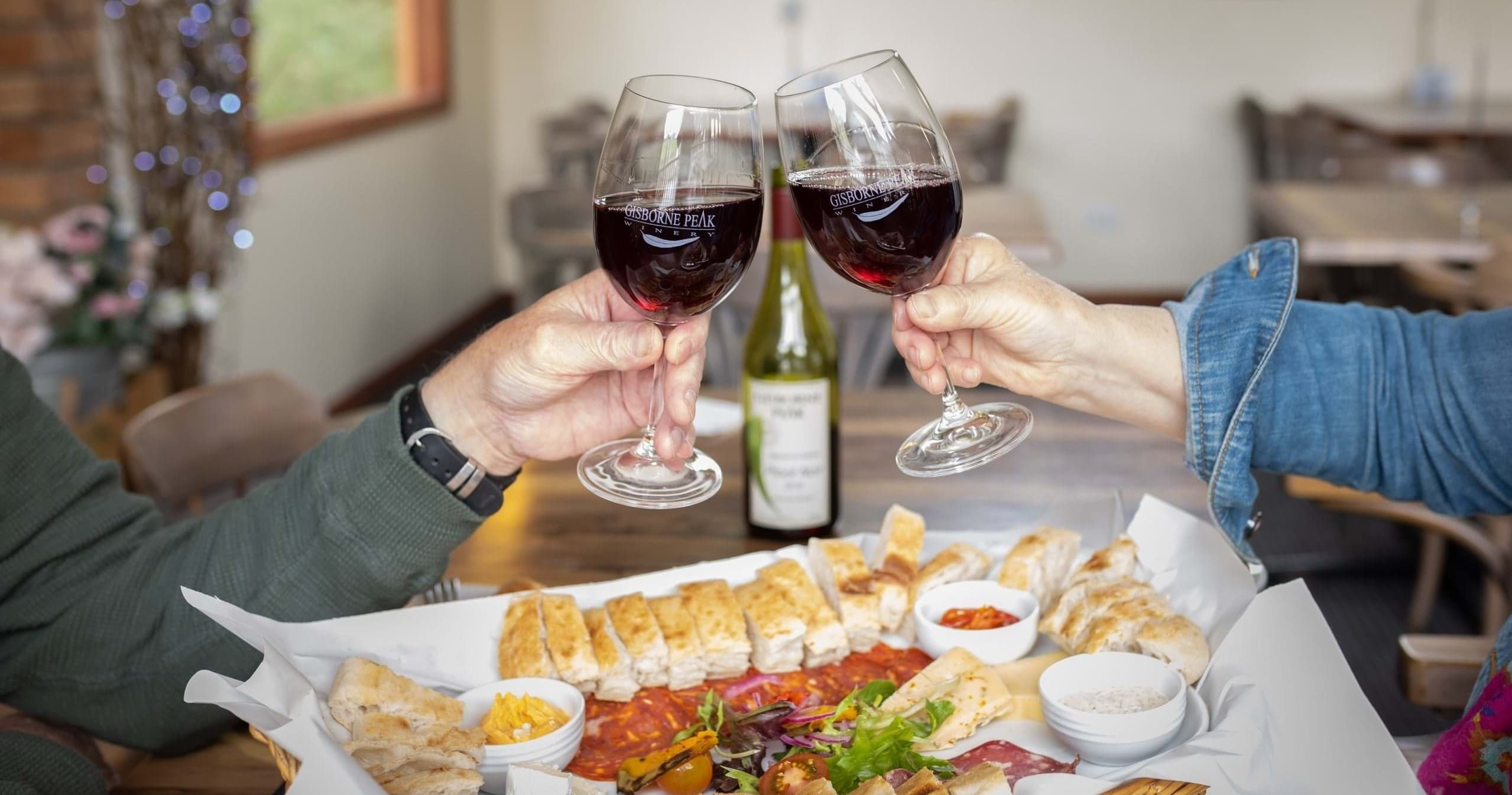 Two people clinking red wine over shared platter indoors