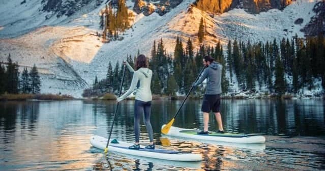 Couple paddleboarding on mountain lake with snowy peaks at sunrise
