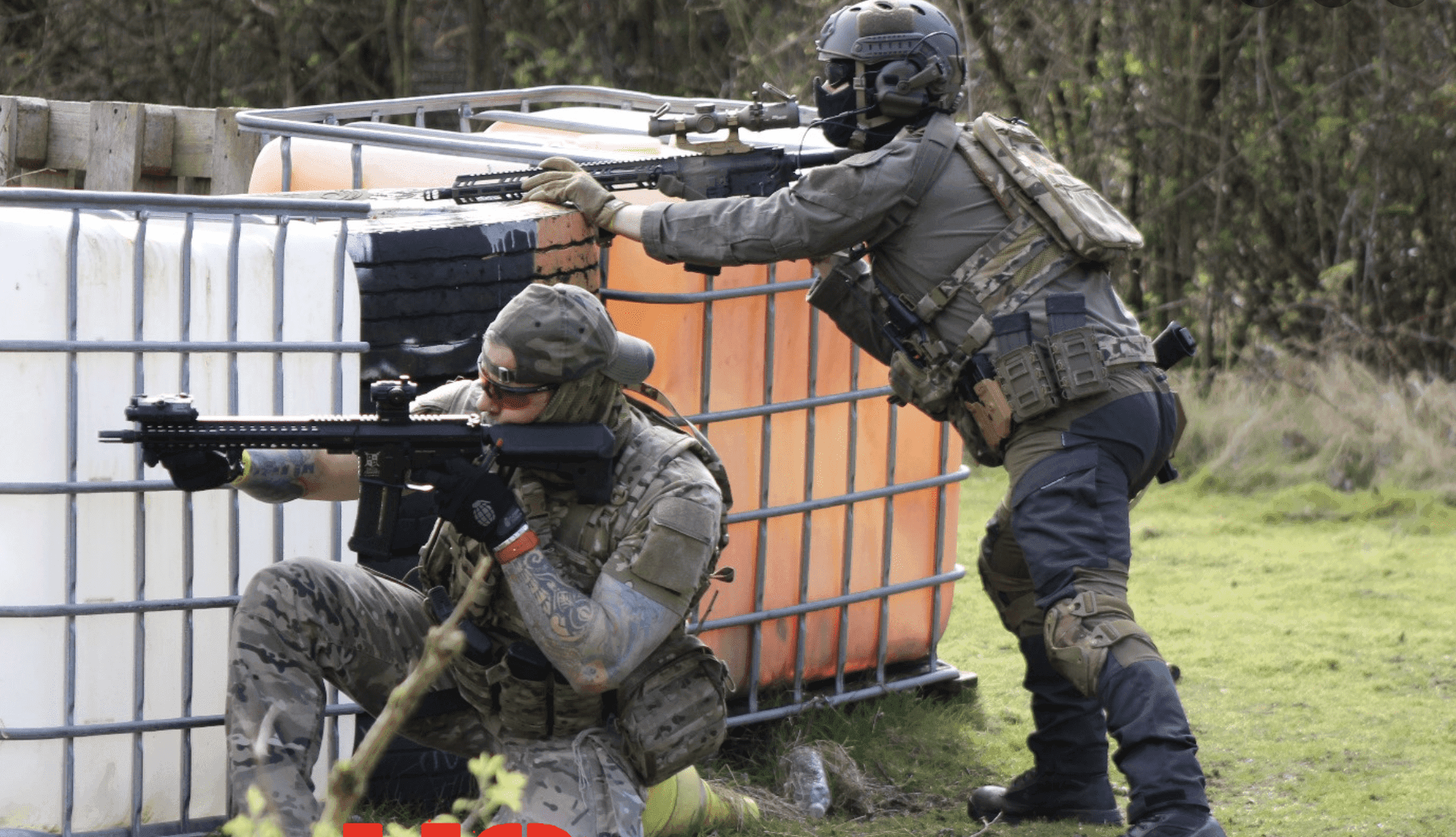 Two airsoft players firing behind barriers in outdoor woodland field