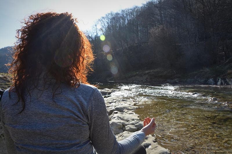Woman meditating riverside at sunset in mountain valley