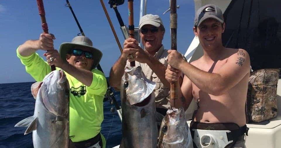 Three anglers displaying large amberjack catches on deep-sea charter