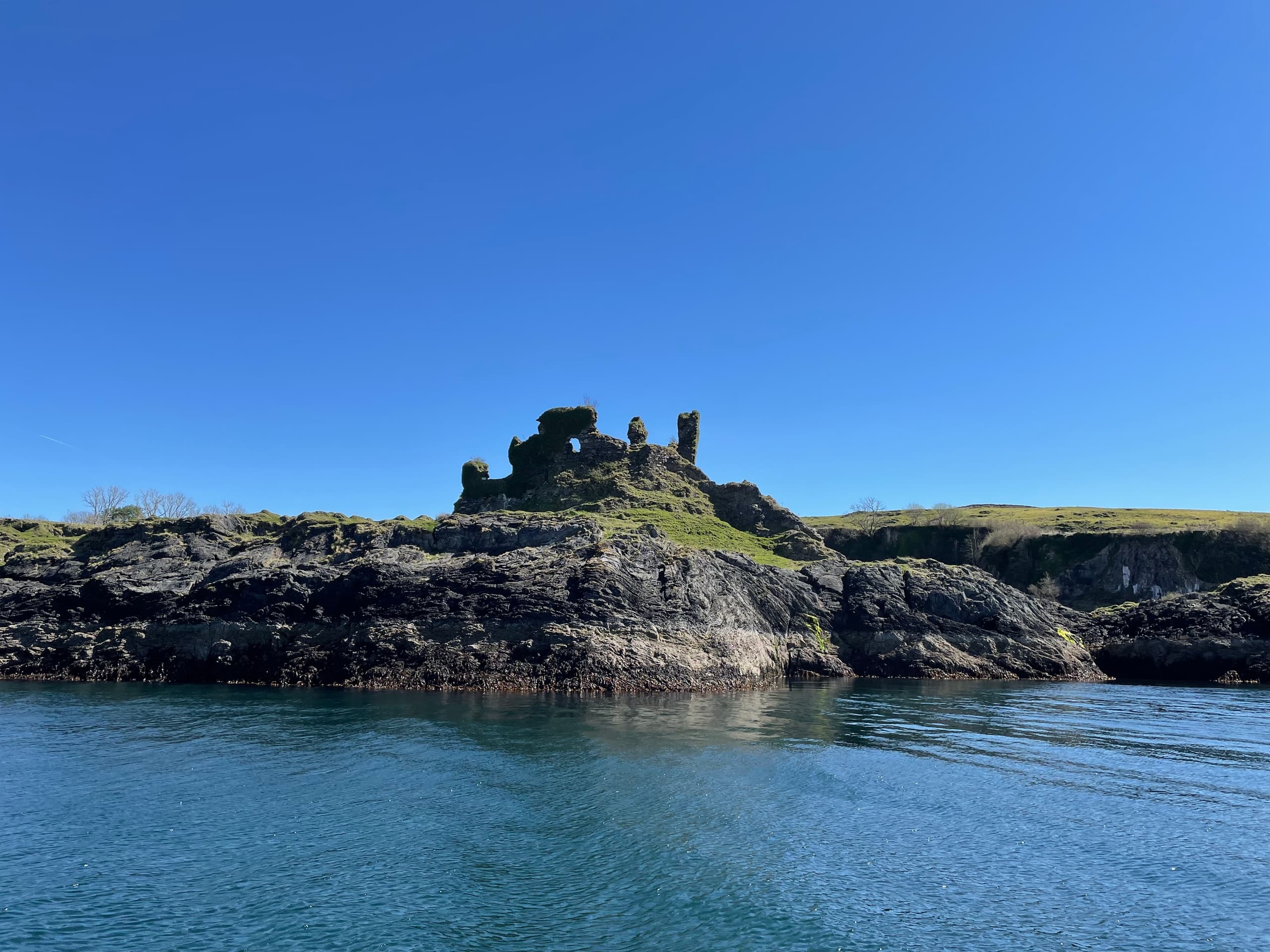 Sightseeing boat approaching ruined castle on rugged Scottish coast