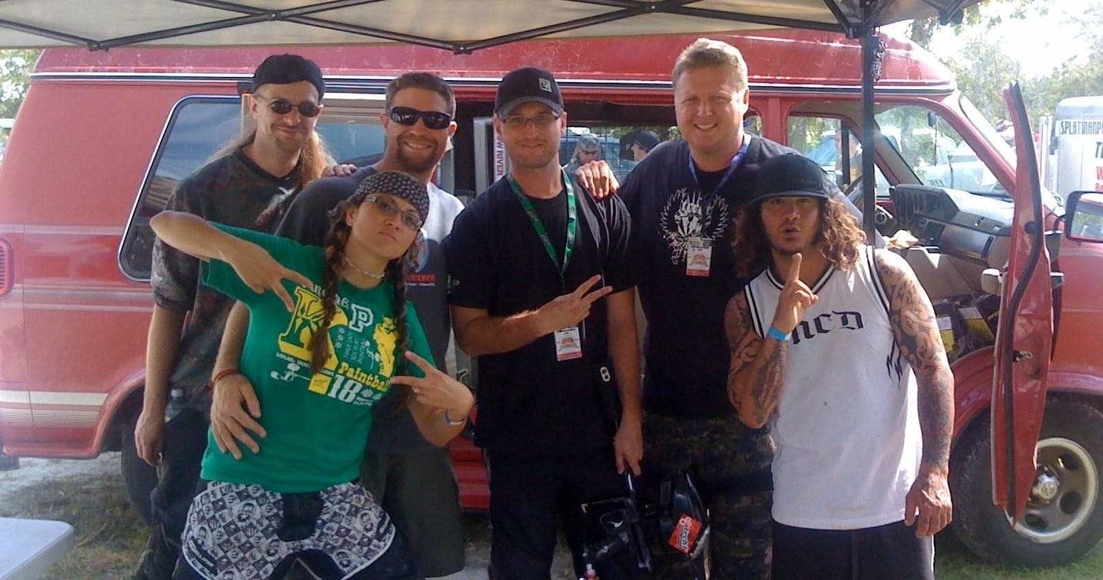 Mixed group posing by red van at outdoor event tent