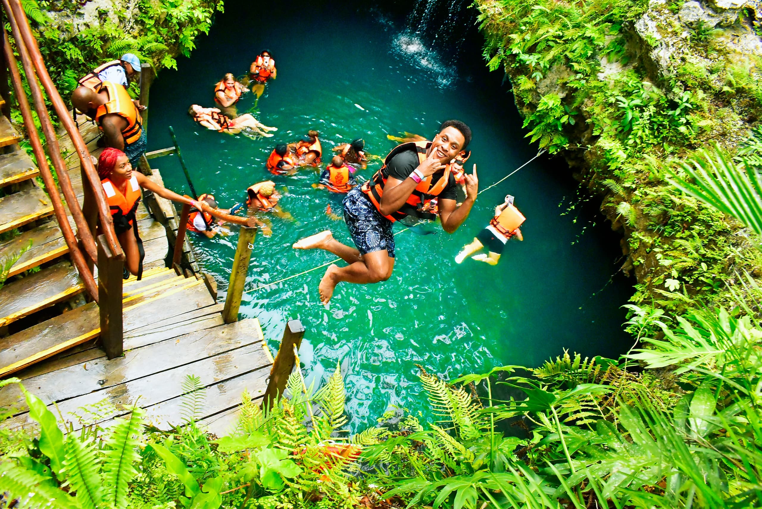 Aerial cenote with swimmers in clear turquoise jungle sinkhole
