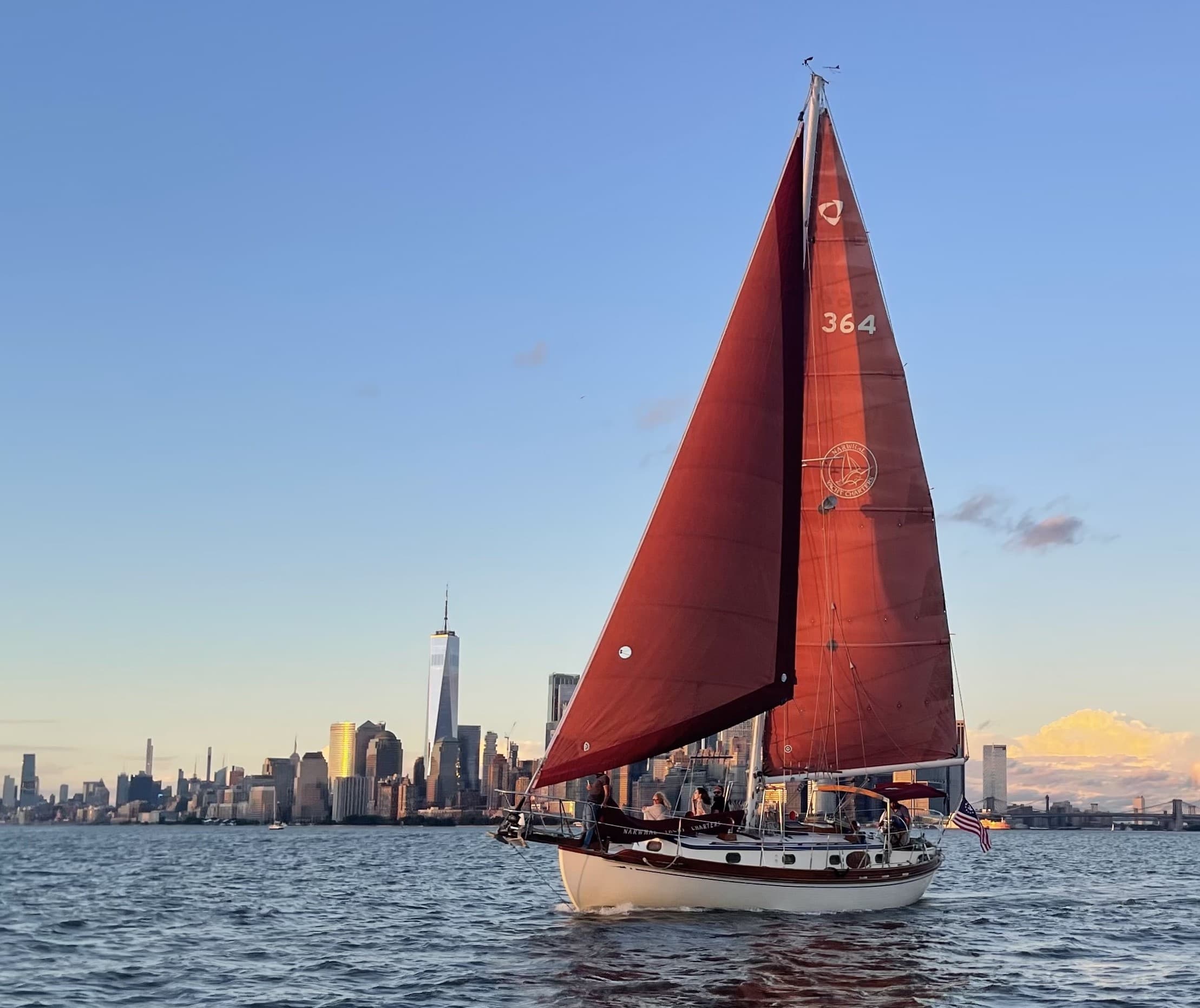 Red sailboat gliding near New York skyline during golden hour