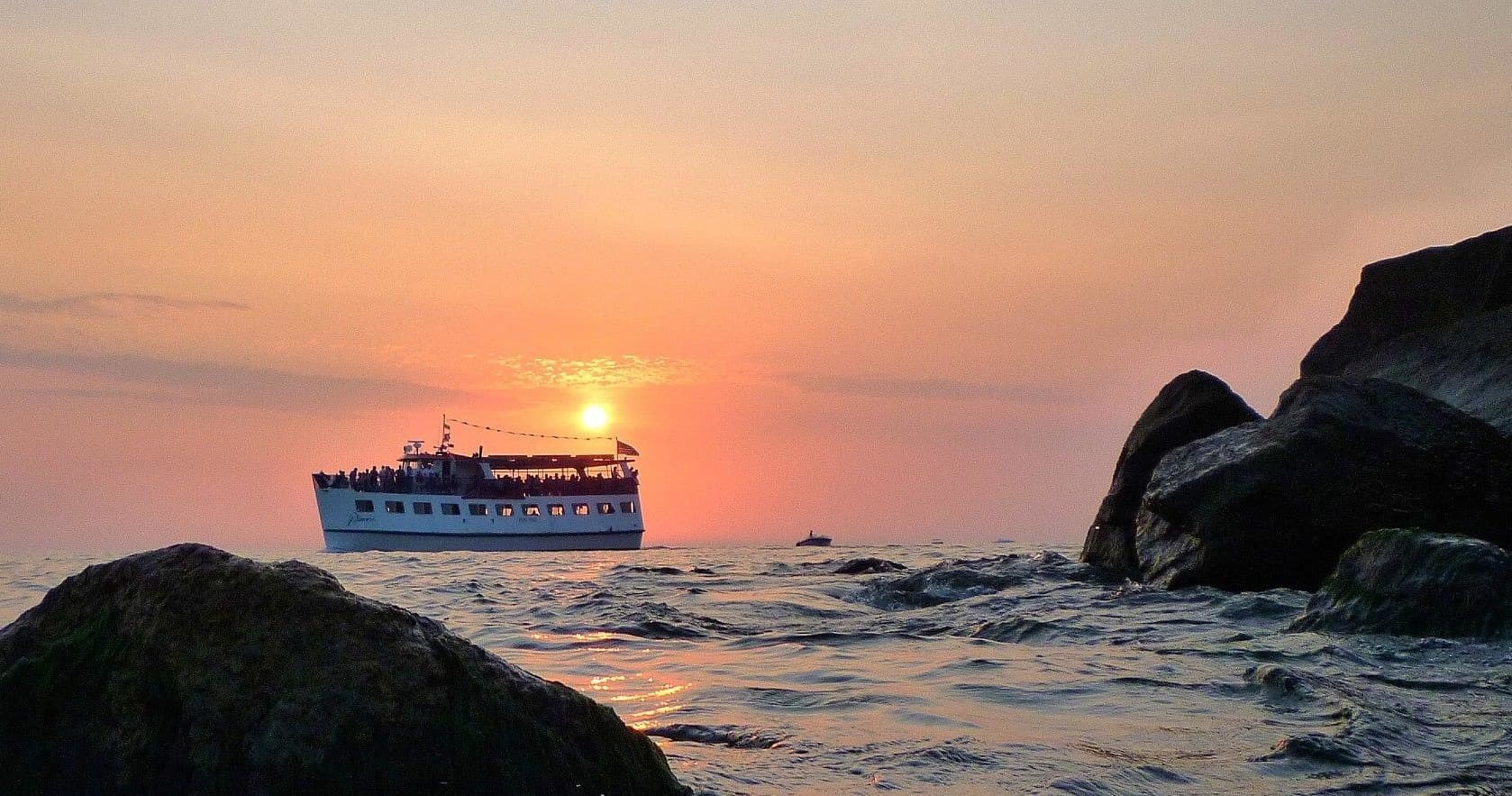 Sunset cruise boat passing rocky coastline at dusk