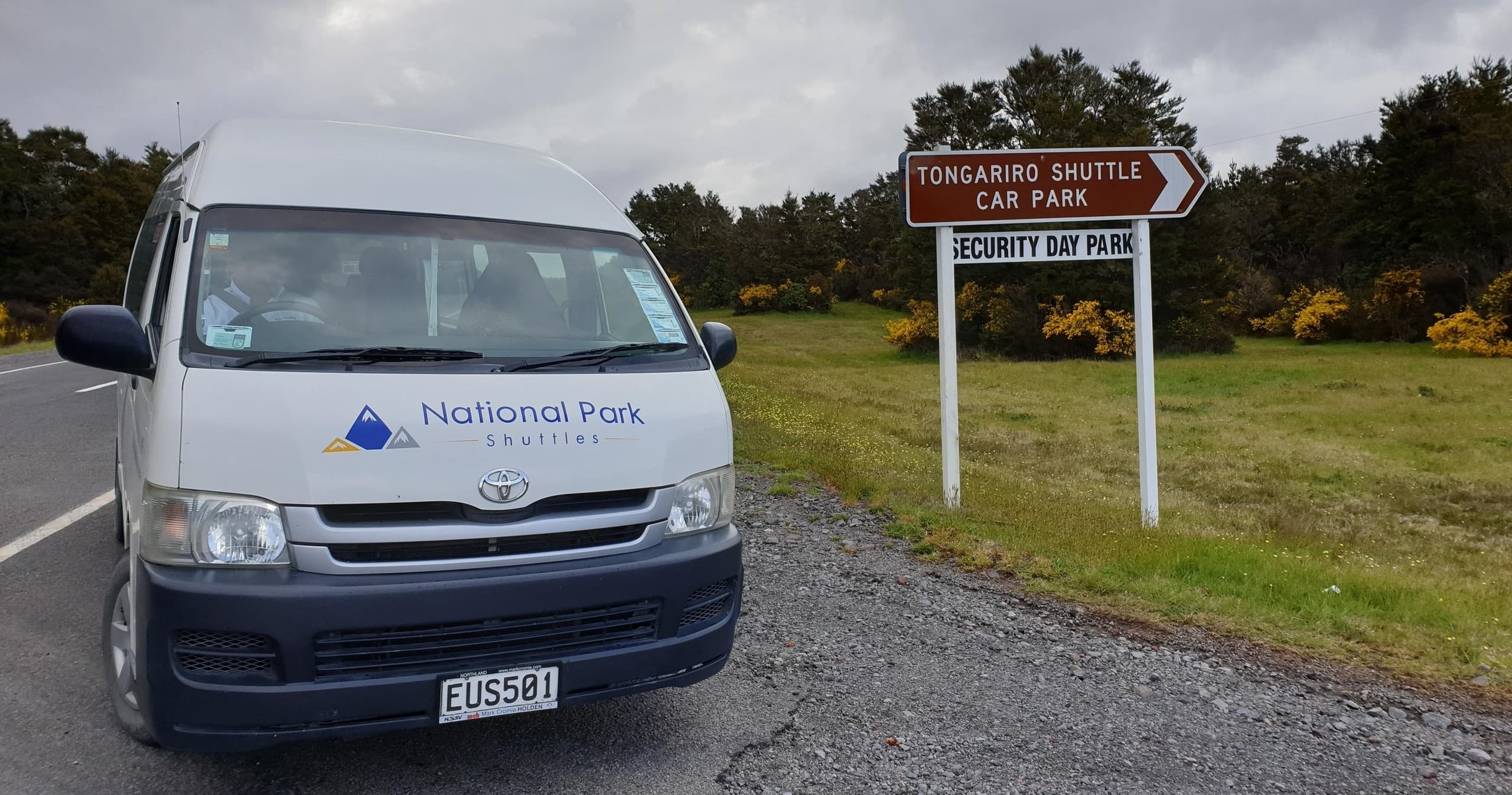 Park shuttle van by Tongariro shuttle sign near alpine road access