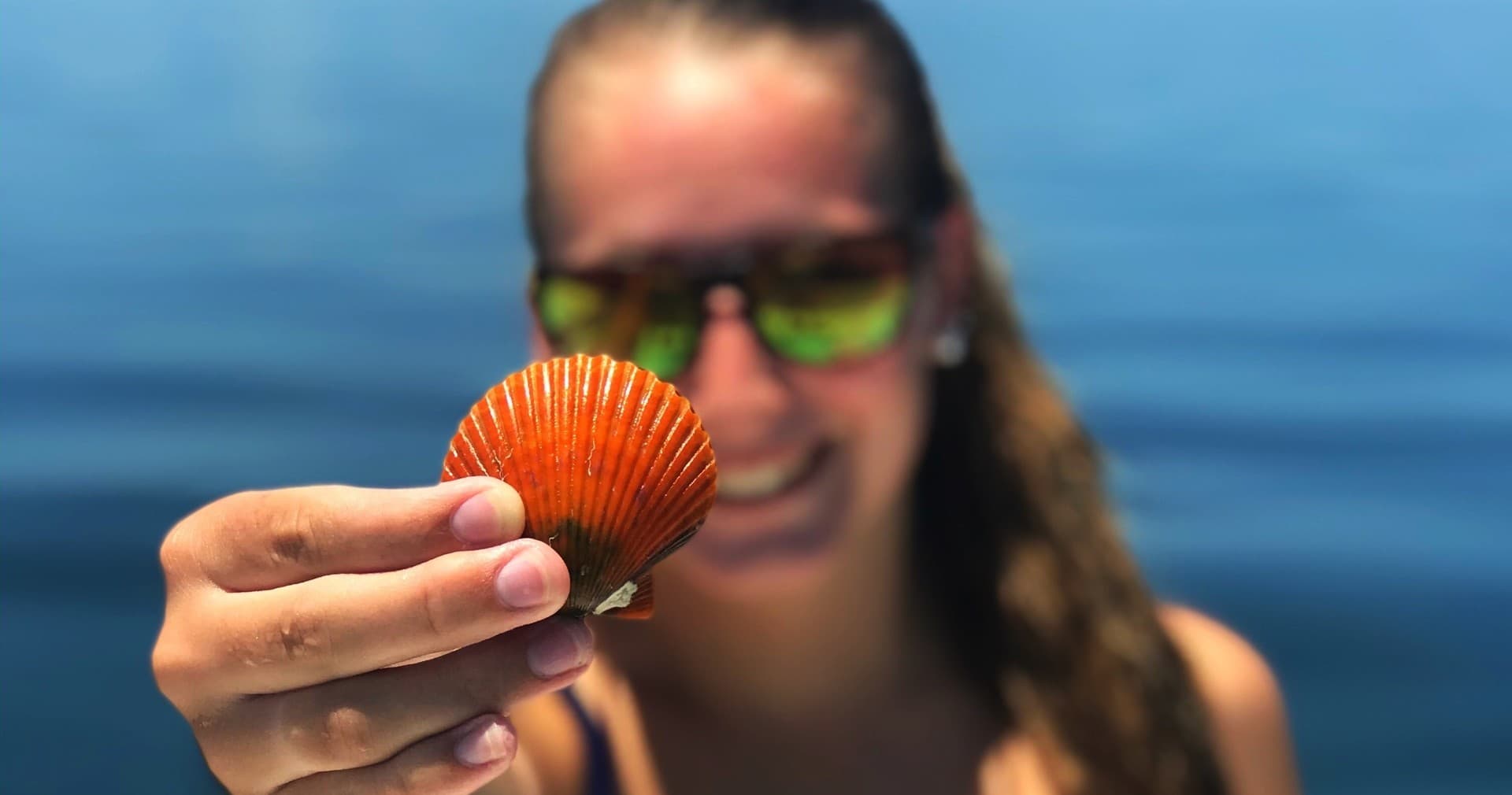 Close-up scallop shell held by angler with ocean backdrop