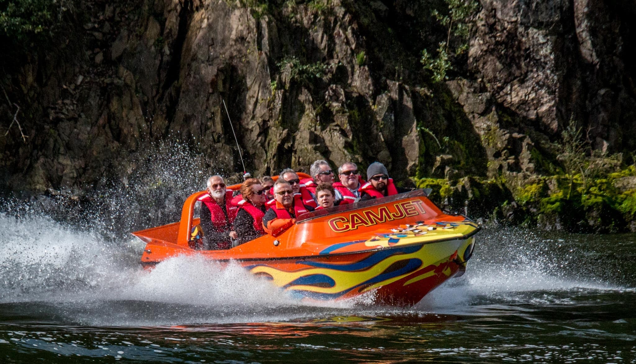 Jetboat carving past cliff and spray near riverside waterfall