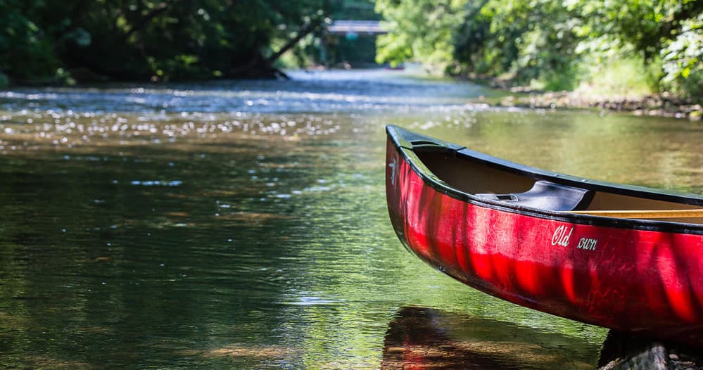Red canoe resting on calm riverbank in shaded forest inlet
