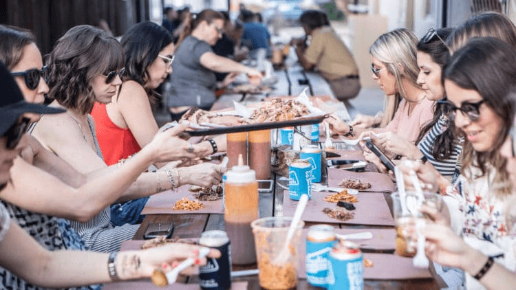 Group dining at long outdoor communal table in Austin streets