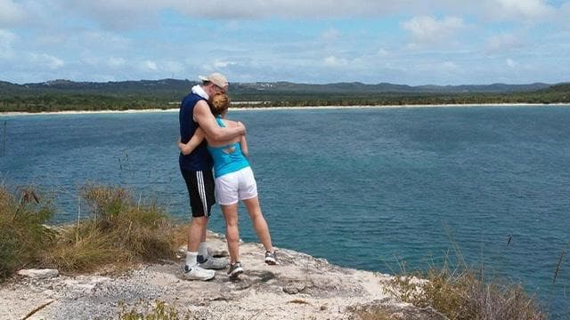 Couple hugging on coastal cliff overlooking ocean bay