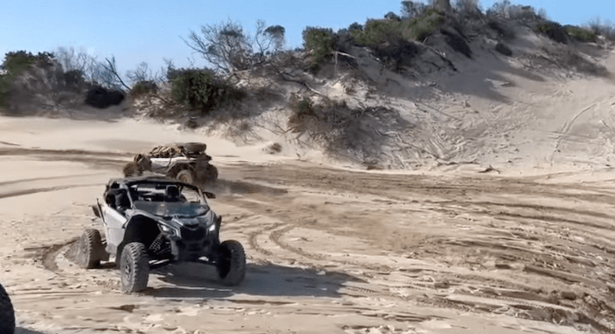 UTV dune buggies driving across sandy coastal dunes at speed