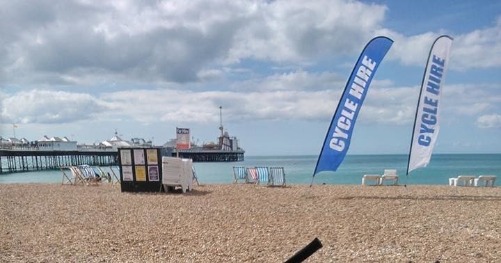 Bike rental flags on Brighton beach with pier and sea