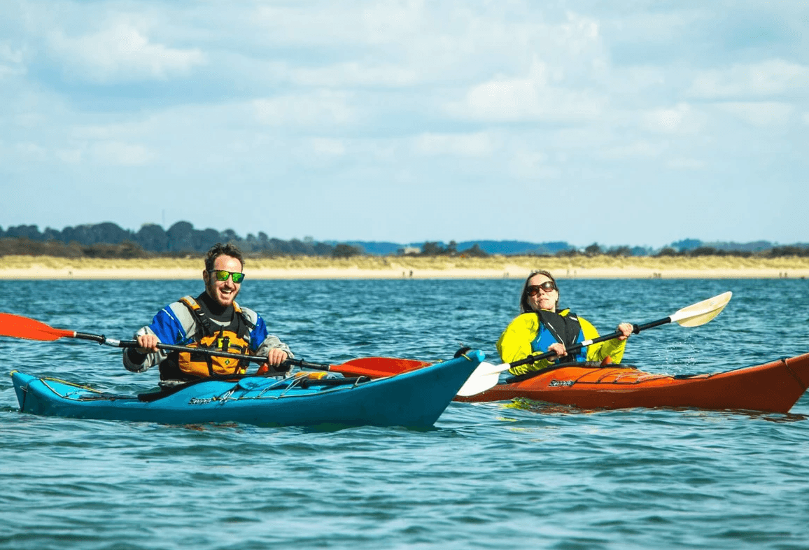 Two sea kayakers paddling near sandy shoreline on calm ocean