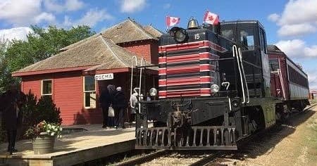 Diesel locomotive at historic prairie station with Canadian flags