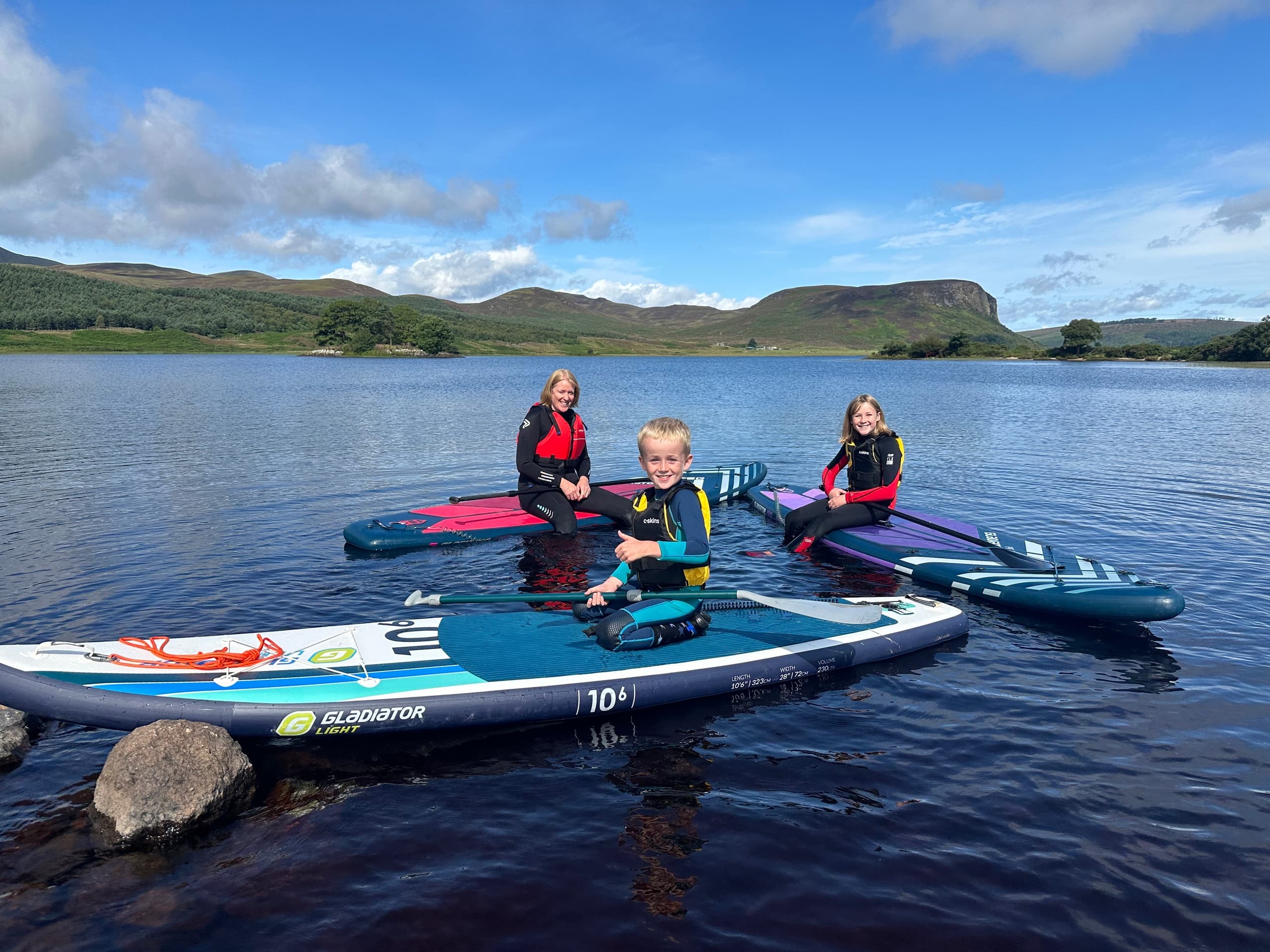 Family paddleboarding on calm Scottish loch with rolling hills